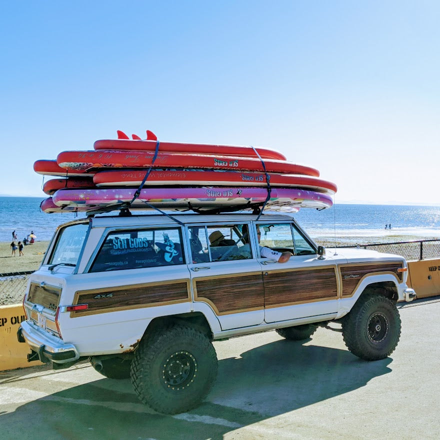 A jeep with paddleboards on the roof sitting at the beach.